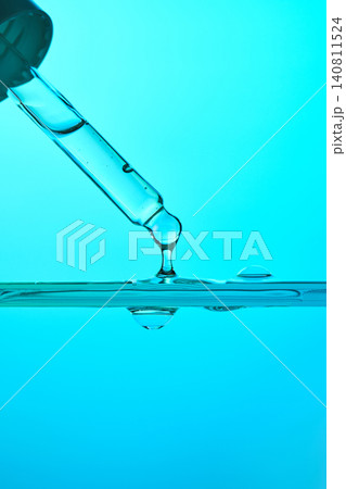 Clear liquid dripping from pipette into water Clear liquid dripping from pipette into water 140811524