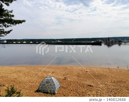 small camouflage tent stands on sandy beach by wide river with barges small camouflage tent stands on sandy beach by wide river with barges 140812688