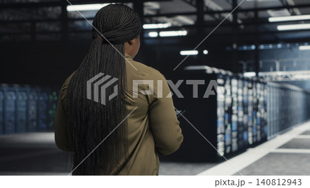 Data center engineer checks server room hardware and network infrastructure with a digital device for stable operations. 140812943