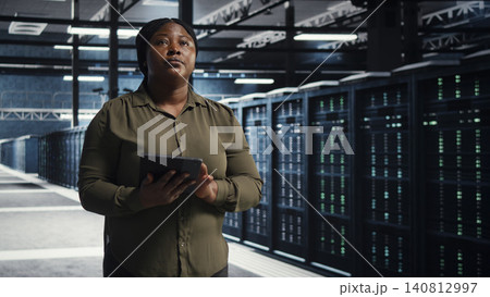 Data center engineer walks through a server room while overseeing IT infrastructure and network operations. Data center engineer walks through a server room while overseeing IT infrastructure and network operations. 140812997