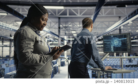 Data center employee monitors operational metrics on mockup PC inside a server room to improve infrastructure performance. 140813015