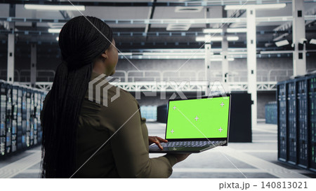 Data center engineer uses green screen laptop in a data center to inspect hardware and maintain system stability. 140813021