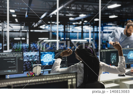 African American woman stretches at a workstation in a server farm to relieve back fatigue after long technical work. African American woman stretches at a workstation in a server farm to relieve back fatigue after long technical work. 140813083