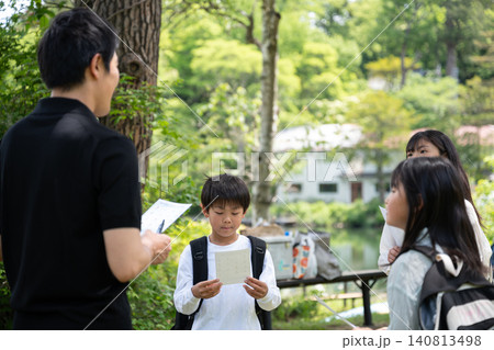 新緑の野外学習で先生の説明を聞く小学生のグループ 新緑の野外学習で先生の説明を聞く小学生のグループ 140813498