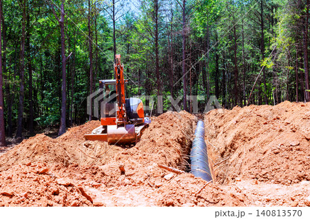 Excavator machine is digging trench in ground surrounded by trees work is for installing septic pipe Excavator machine is digging trench in ground surrounded by trees work is for installing septic pipe 140813570