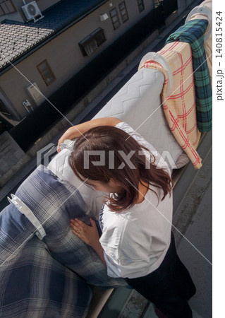 ベランダで布団を干す若い女性(縦位置) ベランダで布団を干す若い女性(縦位置) 140815424
