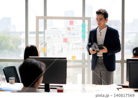 Businessman giving presentation on glass board, manager speaking to diverse team during meeting. Businessman giving presentation on glass board, manager speaking to diverse team during meeting. 140817569
