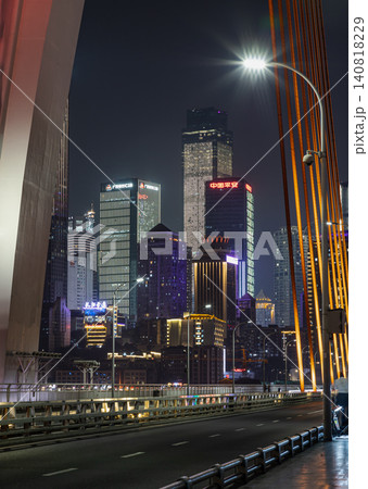 Against the dark night sky of Chongqing, a magnificent tapestry of towering skyscrapers illuminated in ruby and sapphire rises majestically behind the elegant, glowing orange cables and starburst 140818229