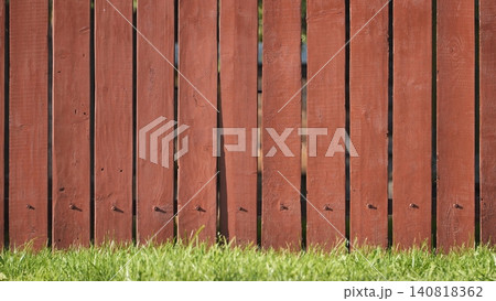 Red wooden garden fence dividing property, featuring grass along its base Red wooden garden fence dividing property, featuring grass along its base 140818362