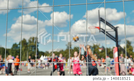 View of an outdoor streetball game through a chain link fence with a blurred background. View of an outdoor streetball game through a chain link fence with a blurred background. 140818521