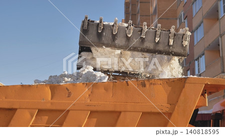 Excavator loading snow onto dump truck, cleaning urban streets after blizzard Excavator loading snow onto dump truck, cleaning urban streets after blizzard 140818595