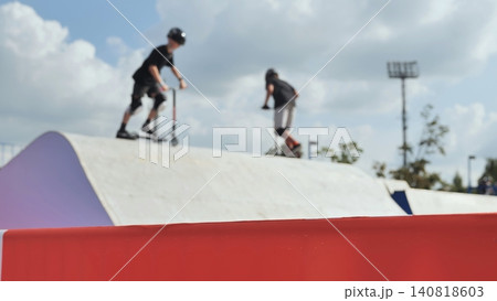 Kids enjoying active summer riding scooters on skatepark ramps under blue sky 140818603