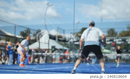 Padel players competing on blue outdoor court viewed through glass wall Padel players competing on blue outdoor court viewed through glass wall 140818604
