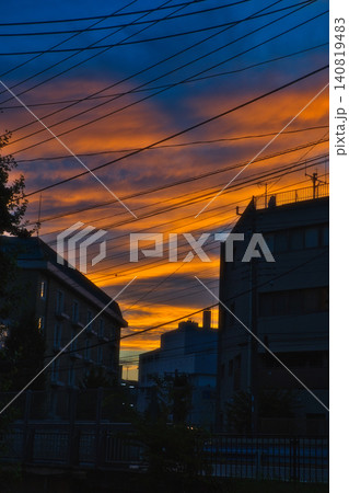 ドラマチックなオレンジ色に染まる雲と夜の訪れを感じる都市の夕暮れ風景 ドラマチックなオレンジ色に染まる雲と夜の訪れを感じる都市の夕暮れ風景 140819483