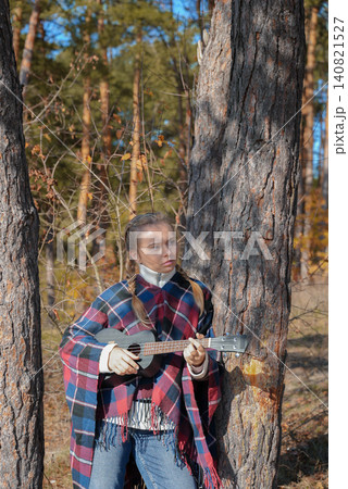 Portrait of smiling caucasian girl plays ukulele in autumnal park. Young woman plays guitar musical instrument outside in nature fall time. Audio music healing Portrait of smiling caucasian girl plays ukulele in autumnal park. Young woman plays guitar musical instrument outside in nature fall time. Audio music healing 140821527