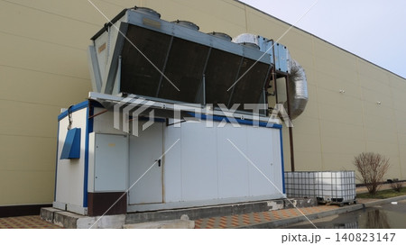 An industrial chiller with a remote V-shaped condenser and axial fans is mounted against the wall. The massive air ducts are insulated with foil. Two Eurocubes for collecting drainage water An industrial chiller with a remote V-shaped condenser and axial fans is mounted against the wall. The massive air ducts are insulated with foil. Two Eurocubes for collecting drainage water 140823147