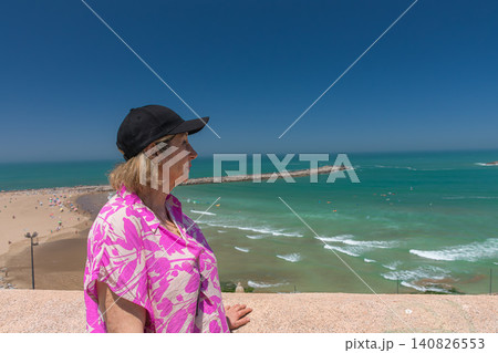 A mature tourist smiles as she gazes at the beach in Rabat and the Bouregreg River from the Kasbah of the Udayas. 140826553
