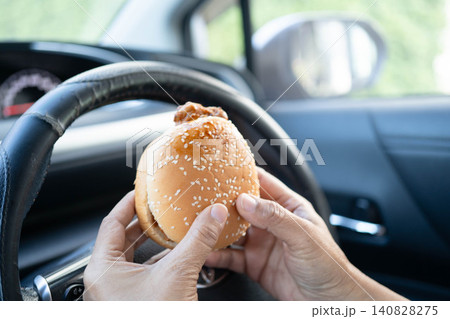 Asian woman driver hold and eat hamburger in car, dangerous and risk an accident. Asian woman driver hold and eat hamburger in car, dangerous and risk an accident. 140828275