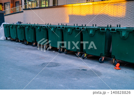 Row of green large wheeled garbage containers lined up on city street at sunset, waste management and urban sanitation concept Row of green large wheeled garbage containers lined up on city street at sunset, waste management and urban sanitation concept 140828826