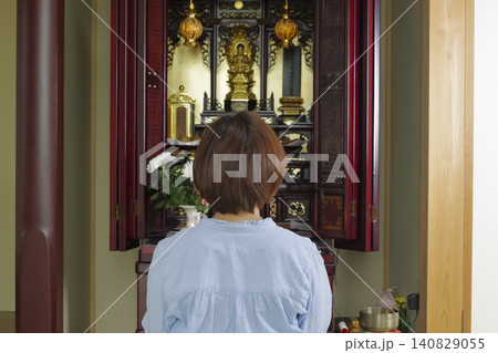 仏壇の前で手を合わせて祈る女性 140829055