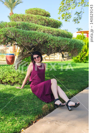 A woman sits playfully on the grass under the canopy of a tree A woman sits playfully on the grass under the canopy of a tree 140829143