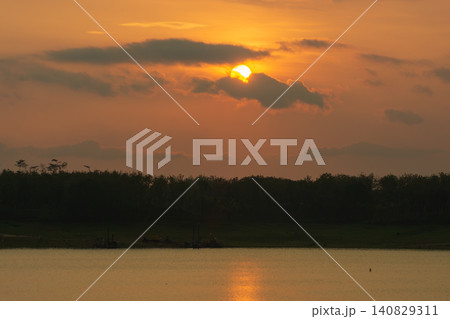 Golden sunset over a calm lake with sun reflection on water surface and forest silhouette 140829311