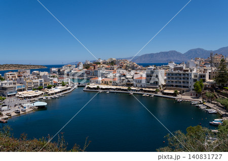 Elevated panoramic view of Lake Voulismeni port and Agios Nikolaos coastal resort city under blue sky, Crete, Greece Elevated panoramic view of Lake Voulismeni port and Agios Nikolaos coastal resort city under blue sky, Crete, Greece 140831727
