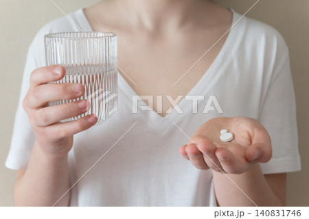 Girl in white clothes take the pill and glass with water in the hand. Healthcare from pharmacy. Kid sit at home because of illness. Girl in white clothes take the pill and glass with water in the hand. Healthcare from pharmacy. Kid sit at home because of illness. 140831746