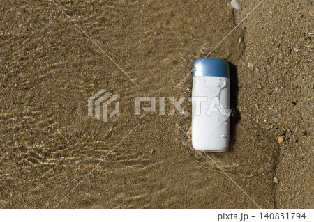 Sunscreen bottle on wet sand with clear water splashes, ideal for summer protection 140831794