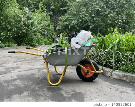 Wheelbarrow loaded with gardening waste and plastic bags in a lush garden setting Wheelbarrow loaded with gardening waste and plastic bags in a lush garden setting 140832601