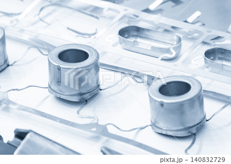 A high-precision metal deep drawing sample part on a strip material in a blue tone scene. 140832729