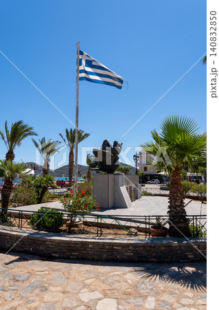 Vertical shot of the Greek war memorial monument with national flag and palm trees in Elounda town square, Crete, Greece Vertical shot of the Greek war memorial monument with national flag and palm trees in Elounda town square, Crete, Greece 140832850