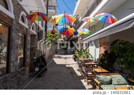 Colorful umbrellas hanging over a narrow street with outdoor cafe tables in Elounda, Crete, Greece Colorful umbrellas hanging over a narrow street with outdoor cafe tables in Elounda, Crete, Greece 140832861