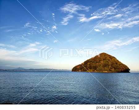 穏やかな青い海に浮かぶ三角形の小島と秋色の木々・青空の絶景 140833255