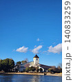 冬晴れの快晴青空と池に面した塔のある白い建物・水鳥が浮かぶ公園風景 140833259