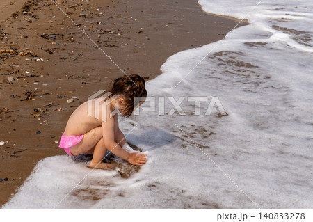 Little girl playing with sea foam on sand beach Little girl playing with sea foam on sand beach 140833278