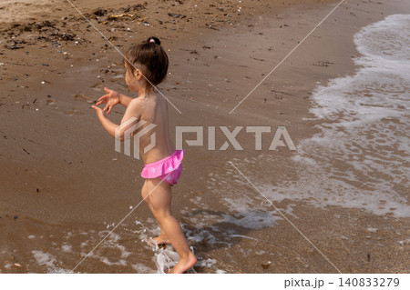 Little girl clapping hands and playing in sea waves on beach Little girl clapping hands and playing in sea waves on beach 140833279