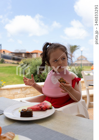 Vertical portrait of cute toddler girl eating dessert on restaurant terrace Vertical portrait of cute toddler girl eating dessert on restaurant terrace 140833291