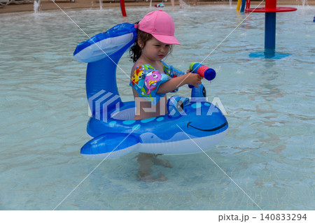 Little girl with water gun toy playing in swimming pool 140833294
