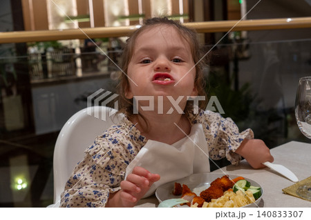 Funny little girl making face with full mouth during dinner in restaurant, silly toddler chewing food and looking at camera, cheeky kid eating nuggets and pasta in high chair Funny little girl making face with full mouth during dinner in restaurant, silly toddler chewing food and looking at camera, cheeky kid eating nuggets and pasta in high chair 140833307