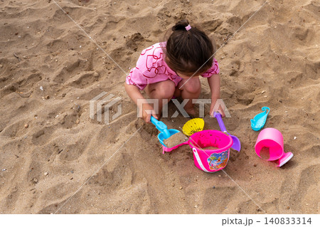 Little girl playing with plastic toys in sand on beach Little girl playing with plastic toys in sand on beach 140833314