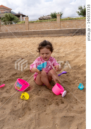 Vertical portrait of little girl playing with plastic sand toys on beach Vertical portrait of little girl playing with plastic sand toys on beach 140833316