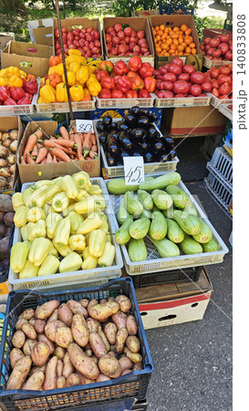 Colorful display of fresh vegetables including potatoes, peppers, cucumbers, and carrots at an outdoor market stall with various produce in baskets 140833808