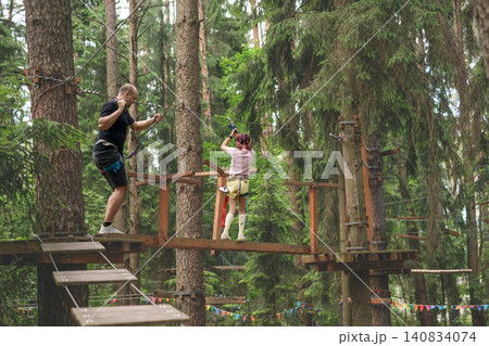 A girl and her father are walking on suspended bridges at high altitudes with obstacles. An amusement park and outdoor activities. Sports education for children A girl and her father are walking on suspended bridges at high altitudes with obstacles. An amusement park and outdoor activities. Sports education for children 140834074