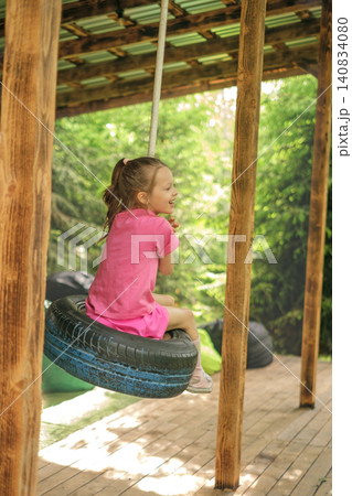A happy child is swinging on a wheel tire suspended from a rope. Children's activities during summer vacations 140834080