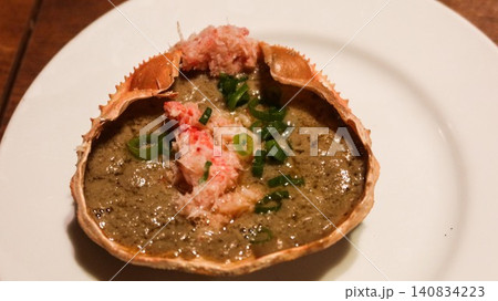 close up of grilled crab shell with kani miso, crab meat, and green onion garnish, which is a traditional Japanese seafood delicacy called Crab Miso on Shell on a white plate with copy space 140834223