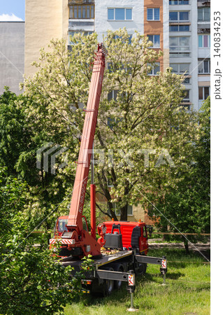 Truck mounted crane standing on grass near blooming trees in city yard 140834253