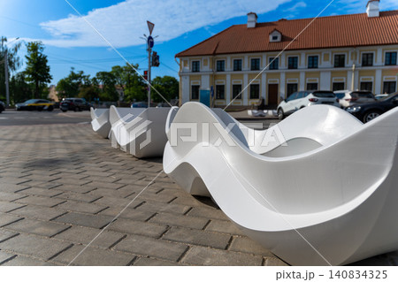 Modern white wave-shaped benches on a paved sidewalk 140834325