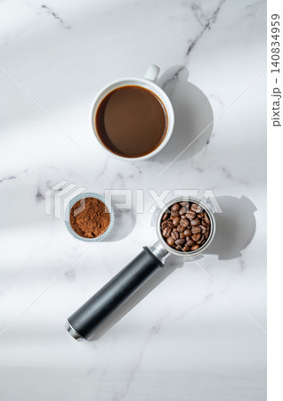 Flat lay of roasted coffee beans in a portafilter, cup of espresso and freshly ground coffee Flat lay of roasted coffee beans in a portafilter, cup of espresso and freshly ground coffee 140834959