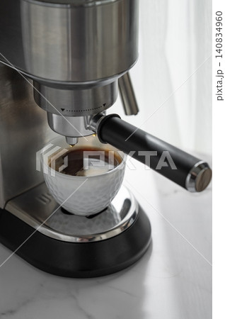 Espresso is brewed into a white cup in a modern coffee machine in soft morning light. Espresso is brewed into a white cup in a modern coffee machine in soft morning light. 140834960